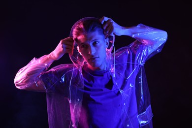 Photo of Young man wearing clear coat on dark background in neon lights