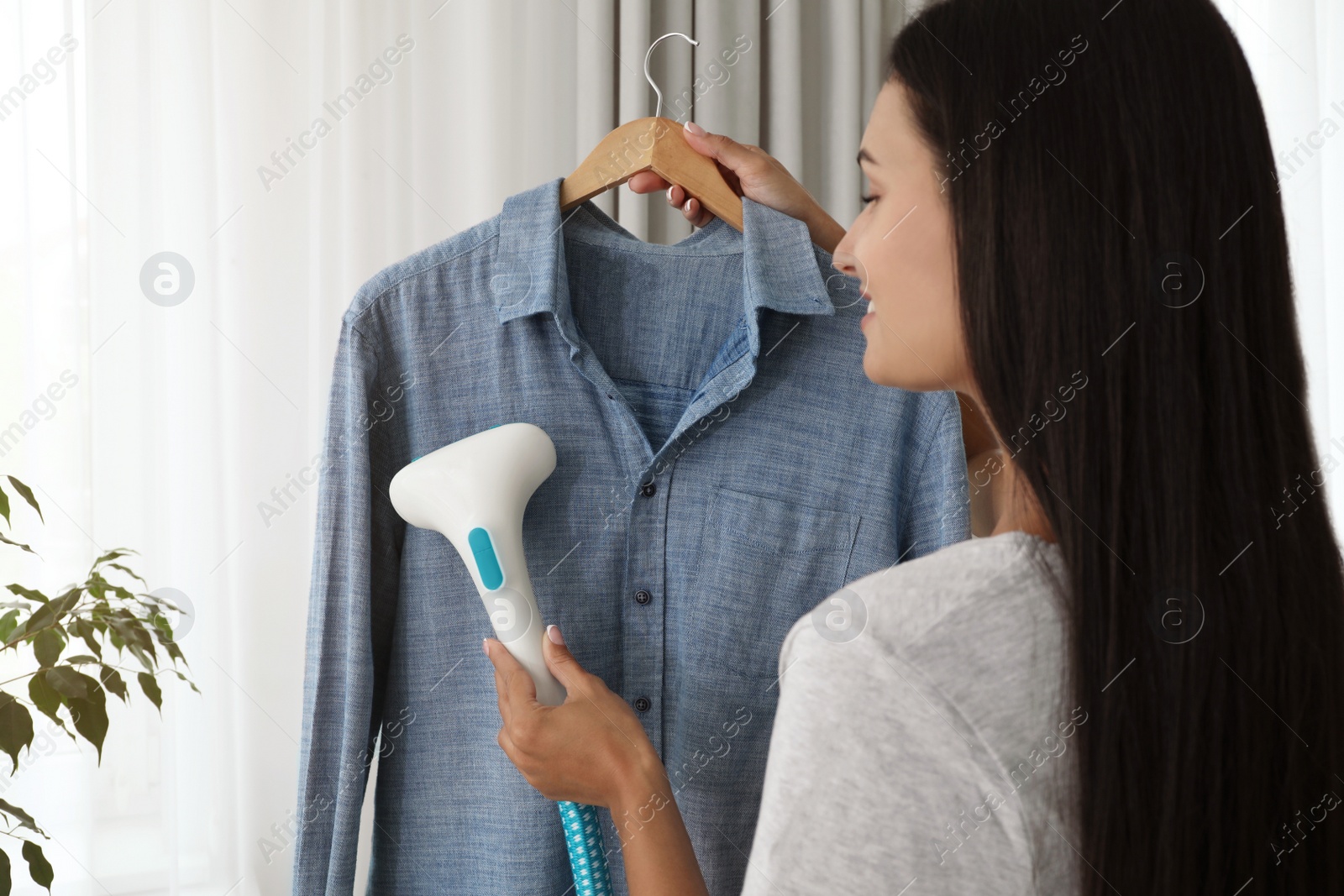 Photo of Woman steaming shirt on hanger at home