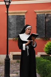 Young nun reading Bible near building outdoors