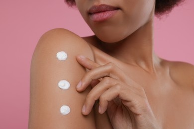 Photo of Young woman applying body cream onto arm on pink background, closeup