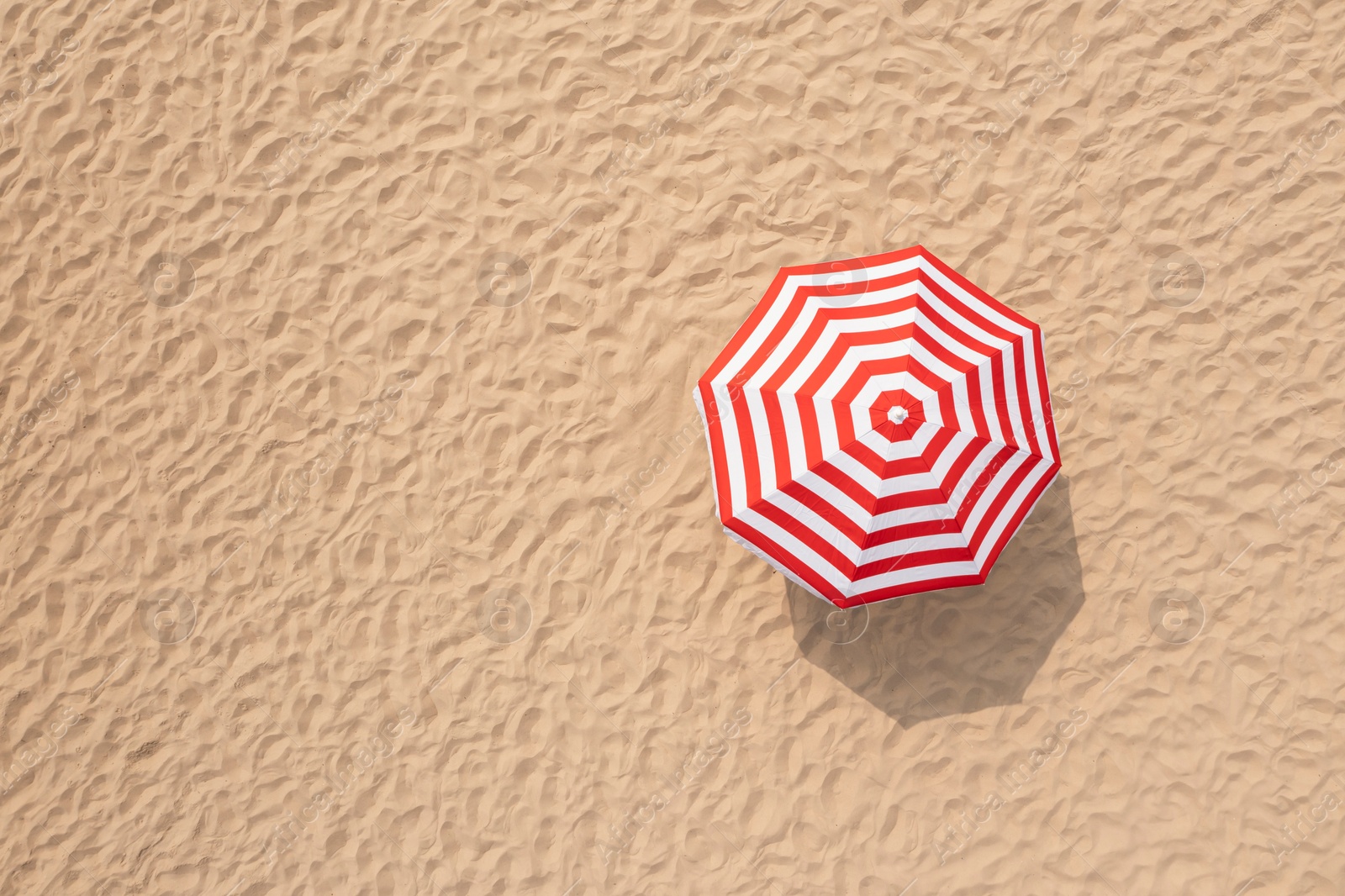 Image of Striped beach umbrella on sandy coast, aerial view. Space for text