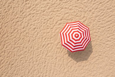 Striped beach umbrella on sandy coast, aerial view. Space for text