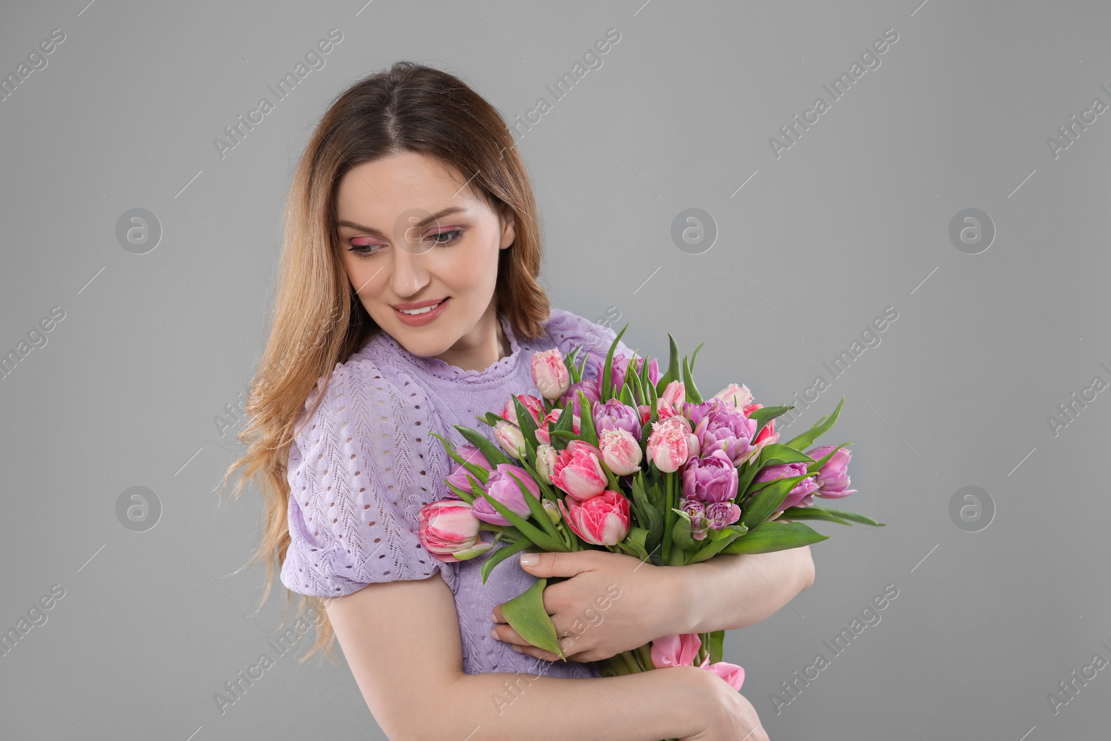 Photo of Happy young woman with bouquet of beautiful tulips on grey background