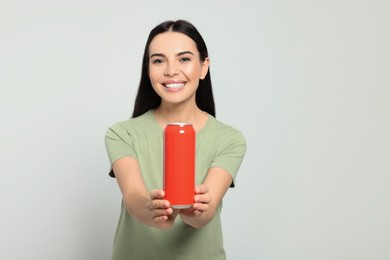 Beautiful happy woman holding red beverage can on light grey background