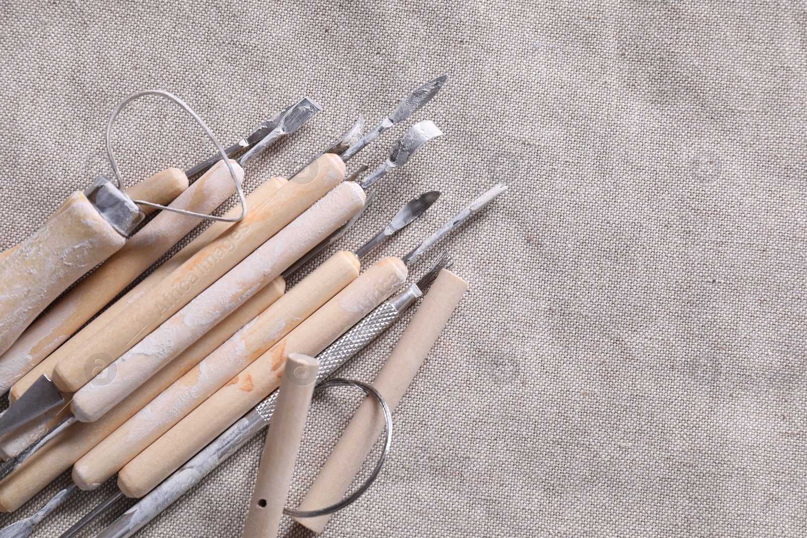 Photo of Set of different clay crafting tools on grey fabric, top view. Space for text