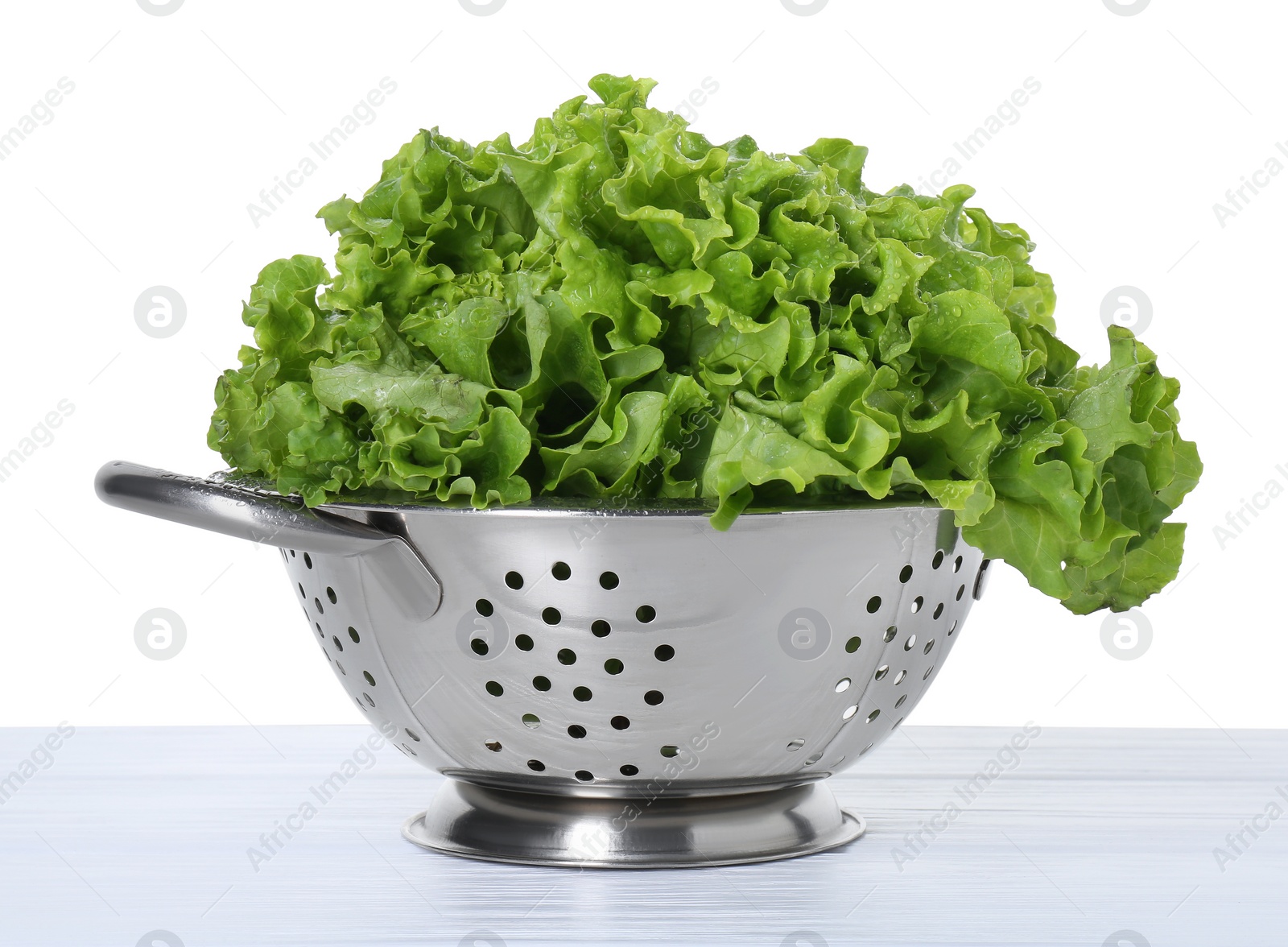 Photo of Metal colander with fresh lettuce on table against white background