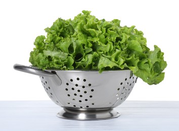 Metal colander with fresh lettuce on table against white background