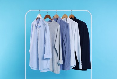 Rack with stylish clothes on wooden hangers against light blue background