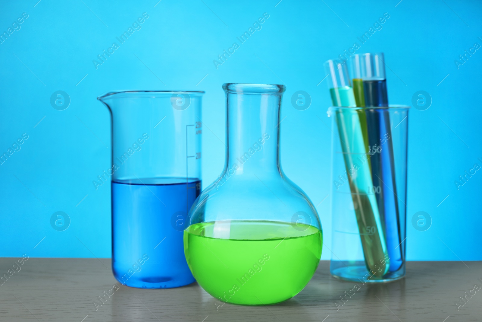 Photo of Different laboratory glassware with colorful liquids on wooden table against light blue background