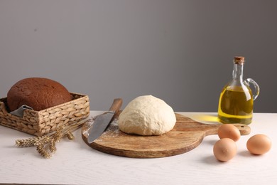 Fresh dough sprinkled with flour and other ingredients on white table near grey wall