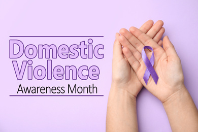 Woman holding purple ribbon on lilac background, top view. Symbol of Domestic Violence Awareness