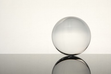 Photo of Transparent glass ball on mirror surface against light background. Space for text