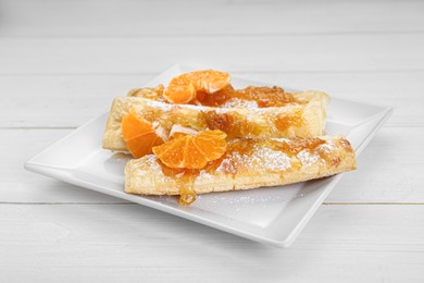 Photo of Fresh tasty puff pastry with sugar powder and tangerines on white wooden table, closeup