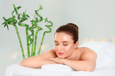 Image of Beautiful young woman relaxing in spa salon. Green bamboo stems on background