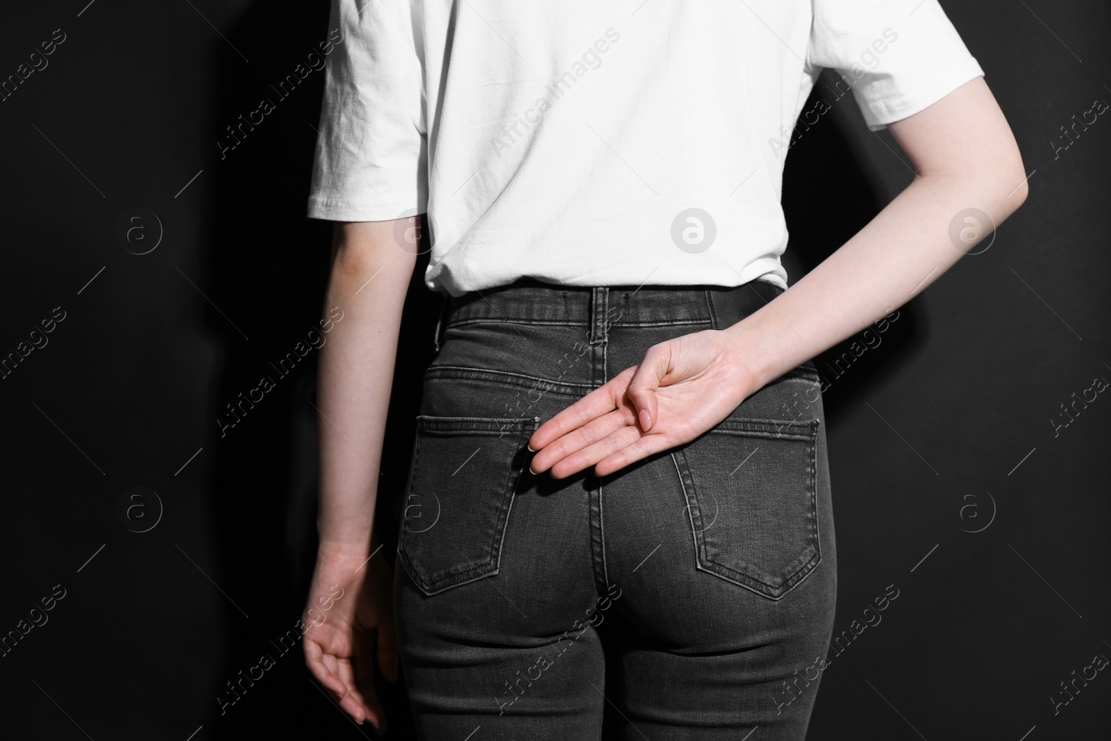 Photo of Woman showing open palm behind her back on black background, back view