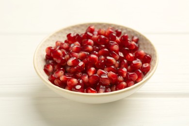 Ripe juicy pomegranate grains in bowl on white wooden table, closeup