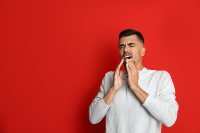 Man sneezing on red background, space for text. Cold symptoms