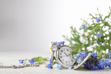 Beautiful blue forget-me-not flowers with pocket watch on light stone table. Space for text