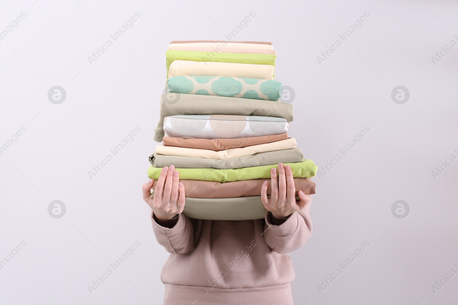 Photo of Woman holding stack of clean bed linens on light background