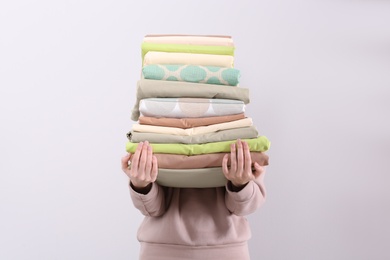 Photo of Woman holding stack of clean bed linens on light background
