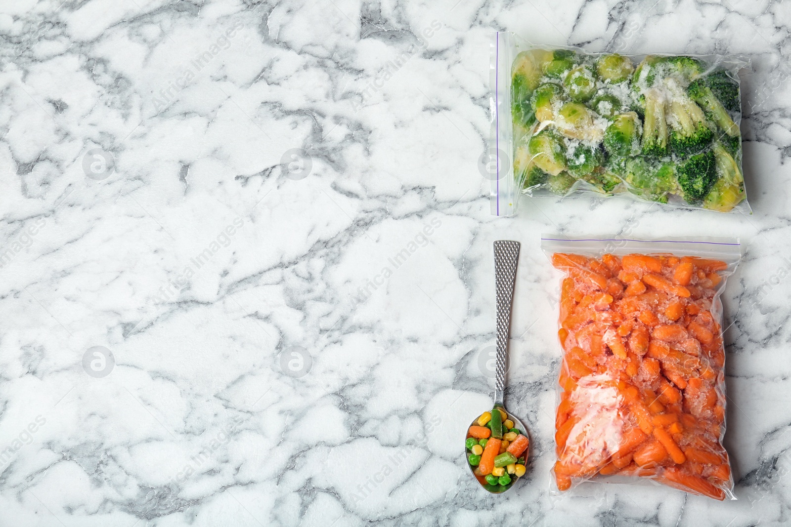 Photo of Plastic bags with frozen vegetables on marble table, top view