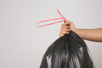 Man holding full garbage bag on light background, closeup. Space for text