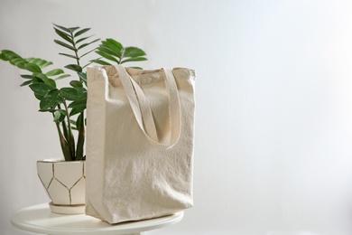 Houseplant and eco bag on table near white wall. Space for text