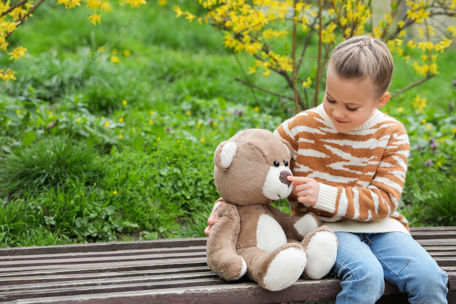 Photo of Little girl with teddy bear on wooden bench outdoors. Space for text