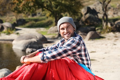 Photo of Male camper in sleeping bag near pond