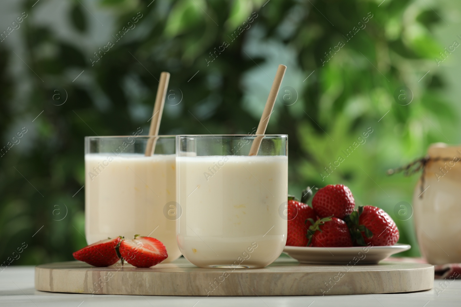 Photo of Tasty yogurt in glasses and strawberries on white wooden table outdoors, closeup