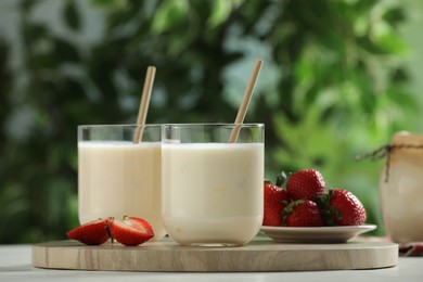 Tasty yogurt in glasses and strawberries on white wooden table outdoors, closeup