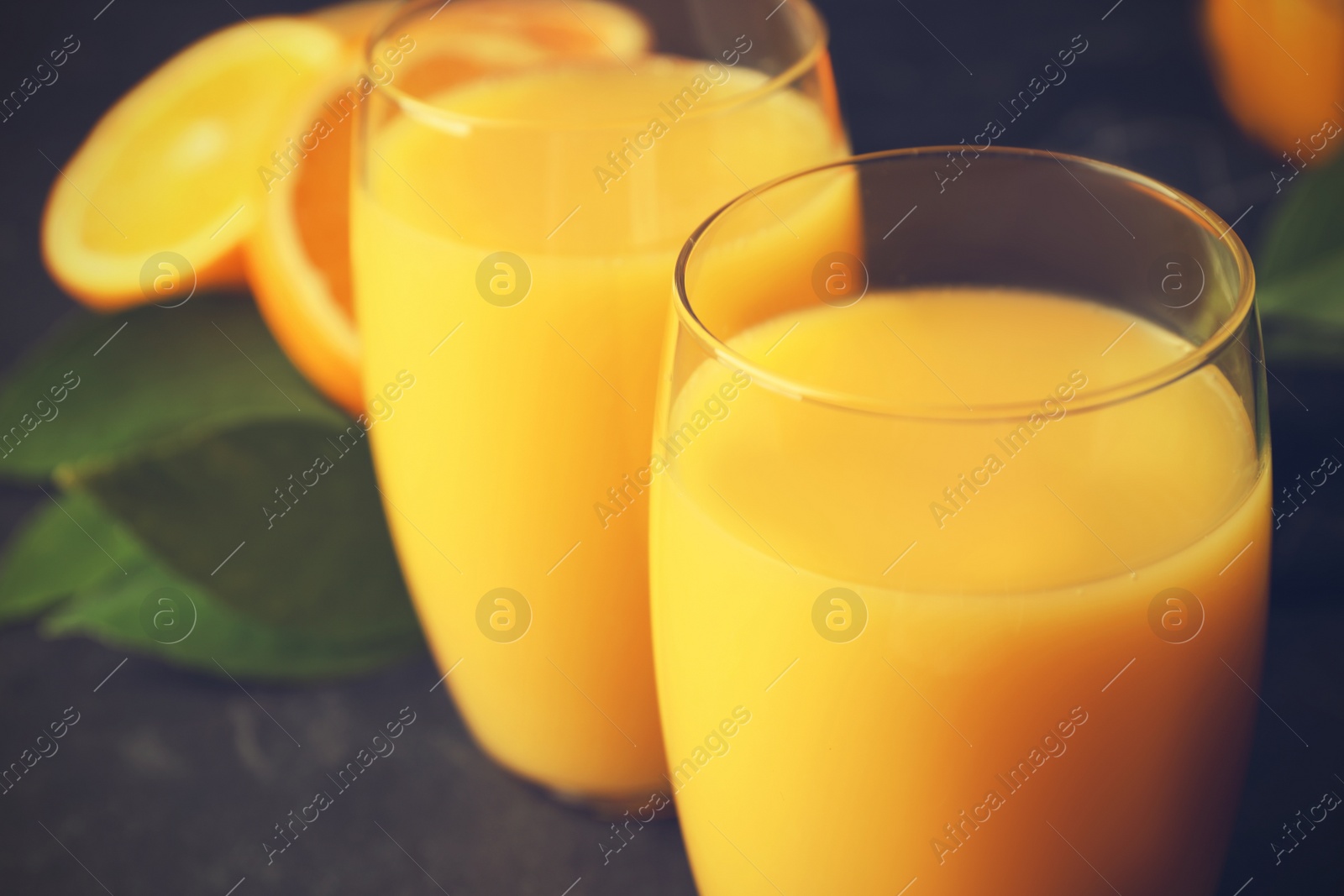 Photo of Glasses of orange juice on black table, closeup