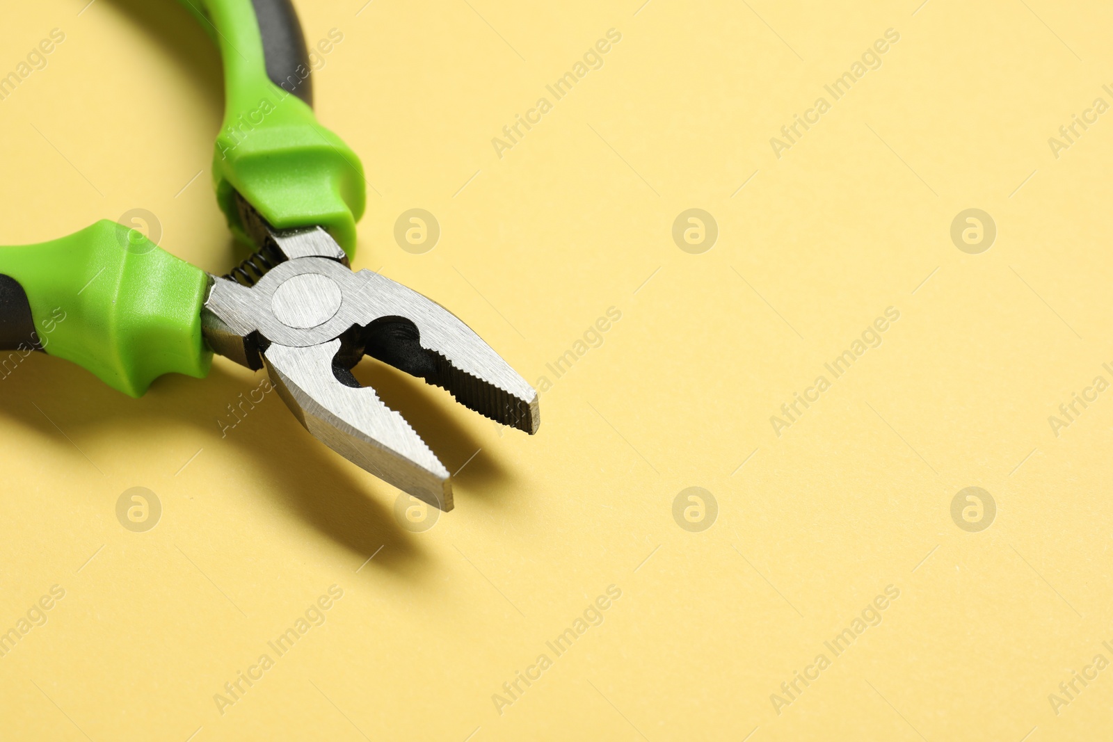 Photo of Combination pliers on yellow background, closeup. Space for text