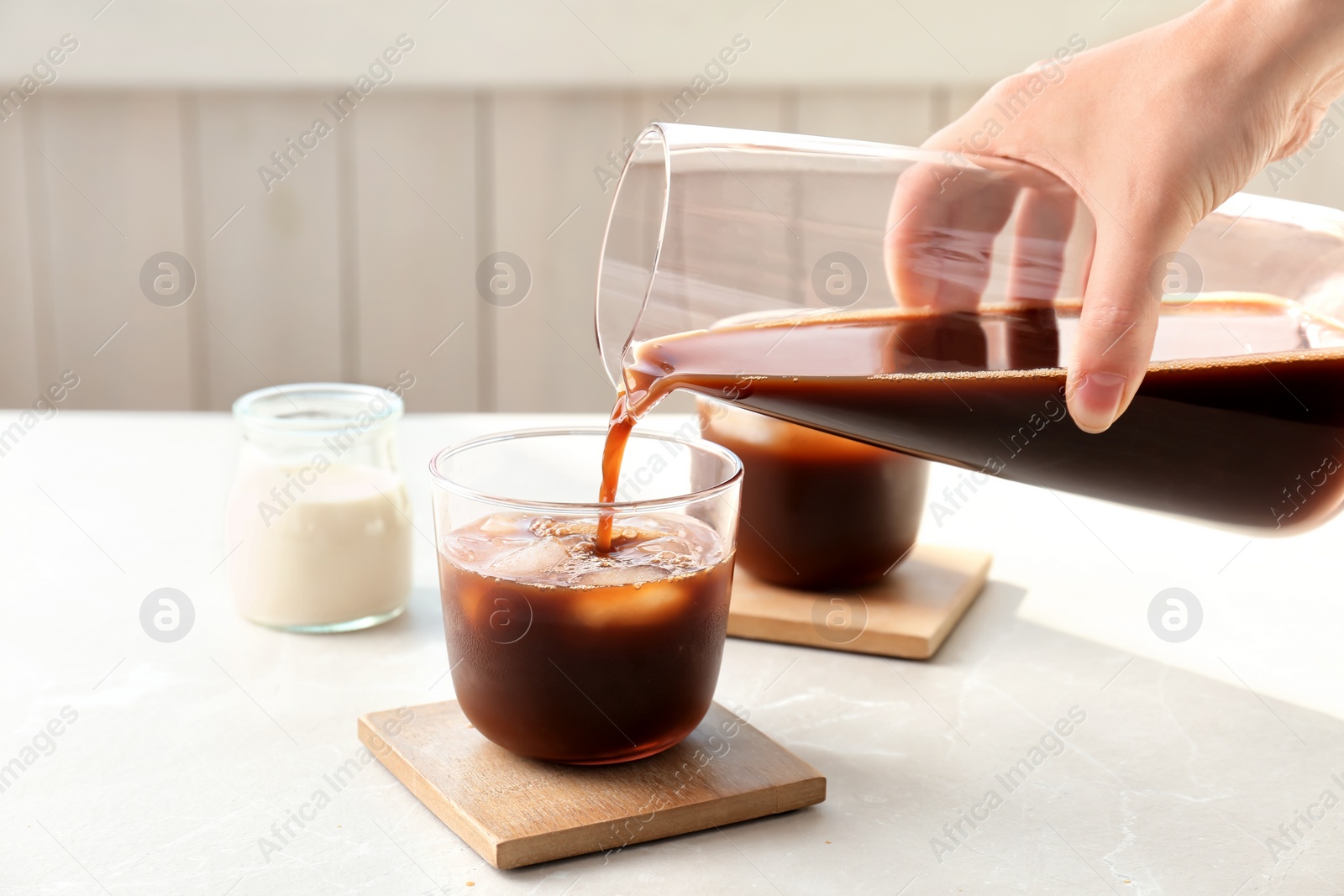 Photo of Woman pouring cold brew coffee into glass on table