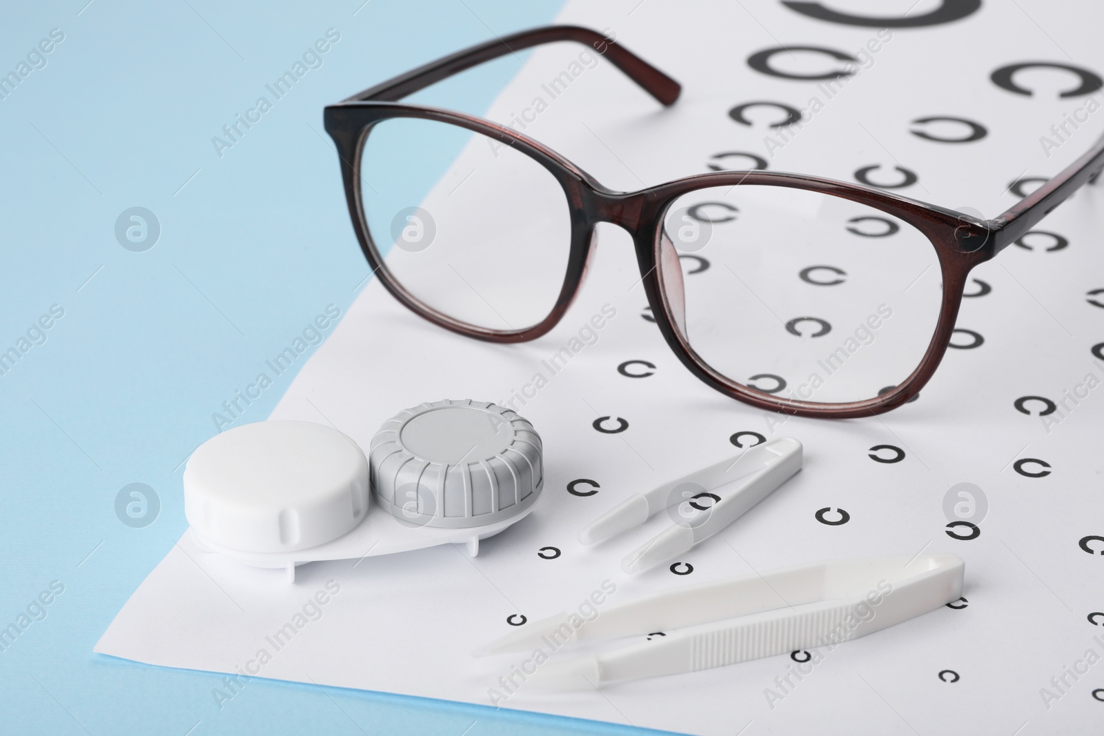 Photo of Vision test chart, glasses, lenses and tweezers on light blue background, closeup
