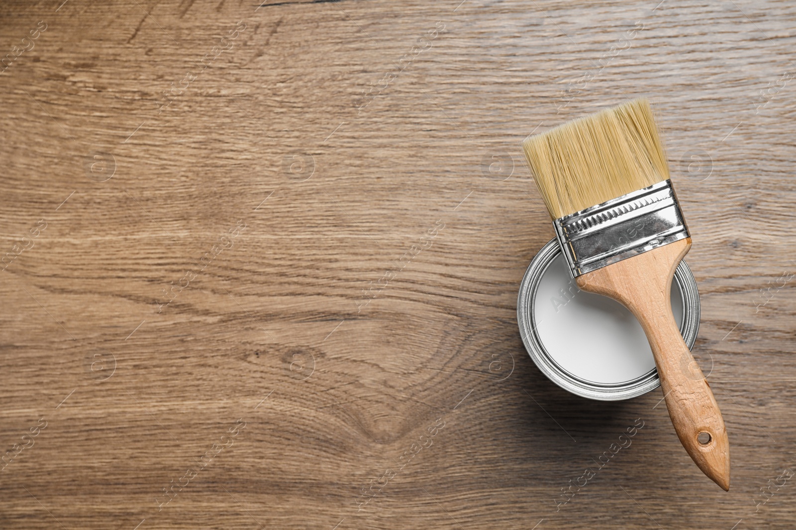 Photo of Open can with white paint and brush on wooden background, top view. Space for text