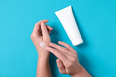 Photo of Woman with tube applying cosmetic cream onto her hand on light blue background, top view