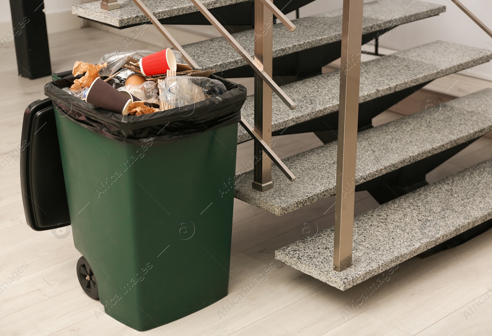 Photo of Full trash bin near stair way indoors. Waste recycling