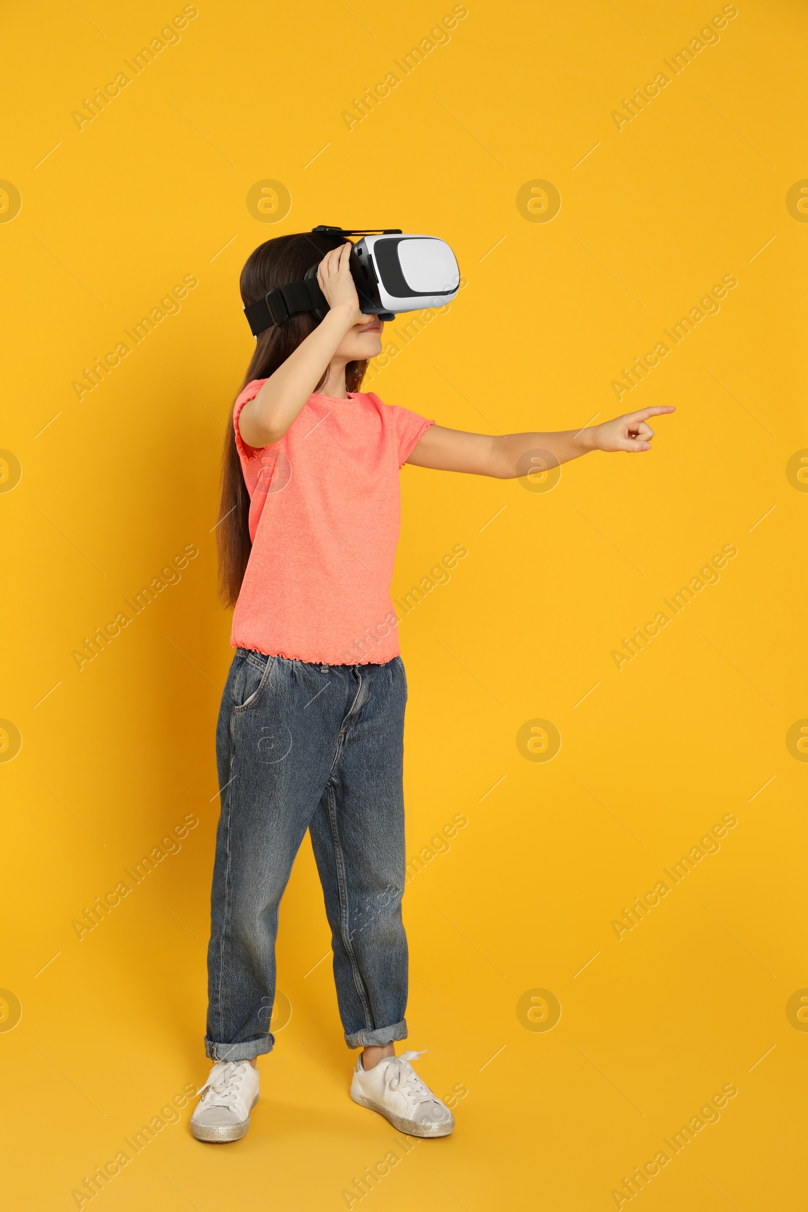 Photo of Little girl using virtual reality headset on yellow background