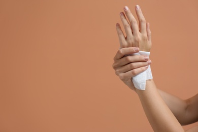 Photo of Woman cleaning hands with paper tissue on light brown background, closeup. Space for text