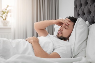 Man suffering from headache while lying on bed at home