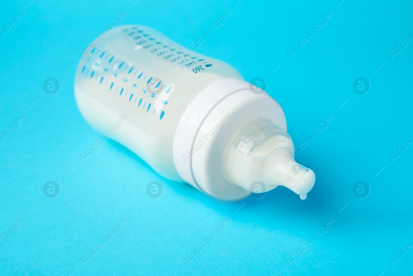 Photo of One feeding bottle with milk on light blue background, closeup