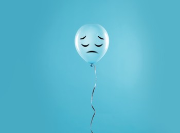 Image of Light blue balloon with sad face on light blue background