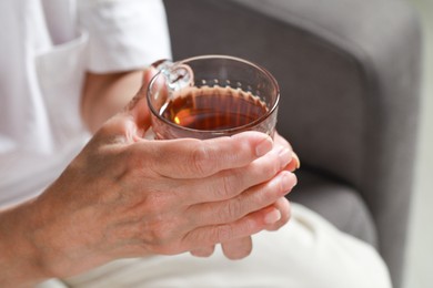 Photo of Elderly woman with cup of hot tea indoors, closeup. Home care service