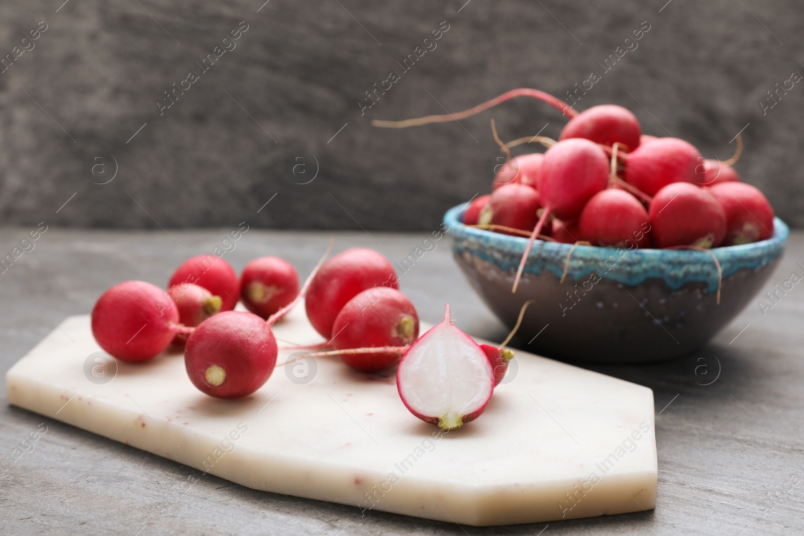 Photo of Board and bowl with fresh ripe radishes on grey table