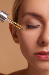 Woman applying cosmetic serum onto her face on beige background, closeup