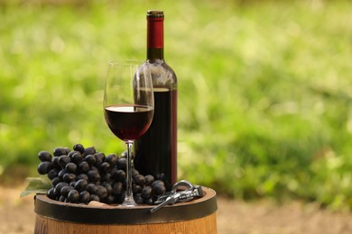 Photo of Delicious wine and ripe grapes on wooden barrel outdoors, space for text