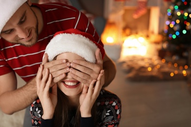 Photo of Young man covering his girlfriend's eyes to make Christmas surprise at home