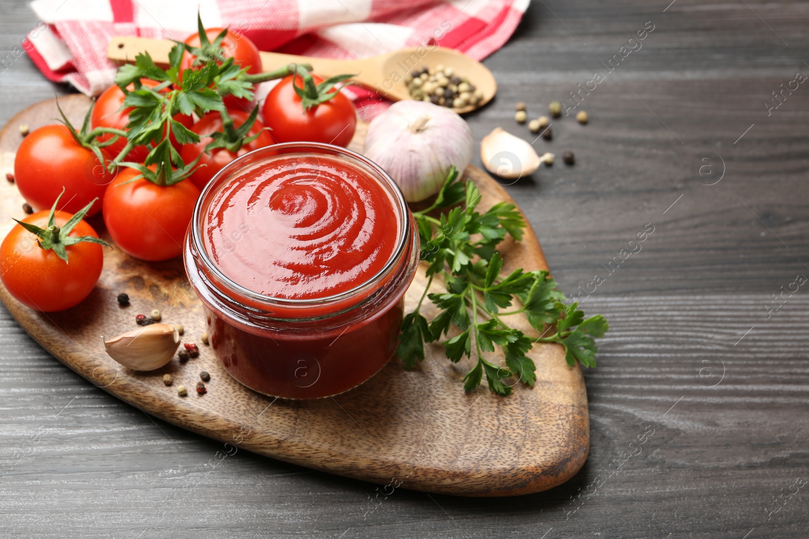 Photo of Tasty ketchup, fresh tomatoes, parsley and spices on grey wooden table, space for text