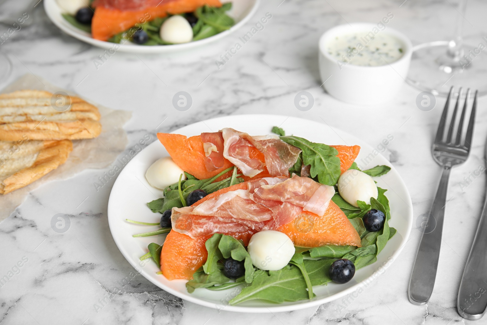 Photo of Fresh melon with prosciutto, mozzarella and arugula on marble table